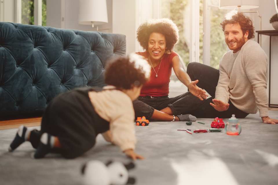 parents playing with child on plush gray carpet in living room with blue velvet couch